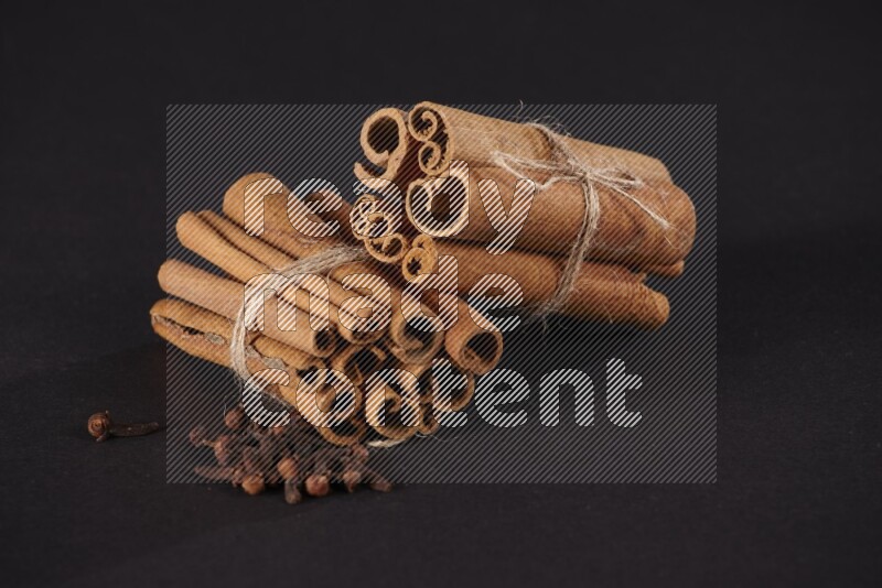 Two bounded stacks of cinnamon sticks with cloves on black background