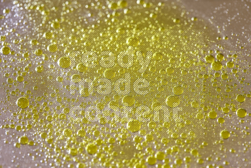 Close-ups of abstract yellow watercolor drops on oil Surface on yellow background