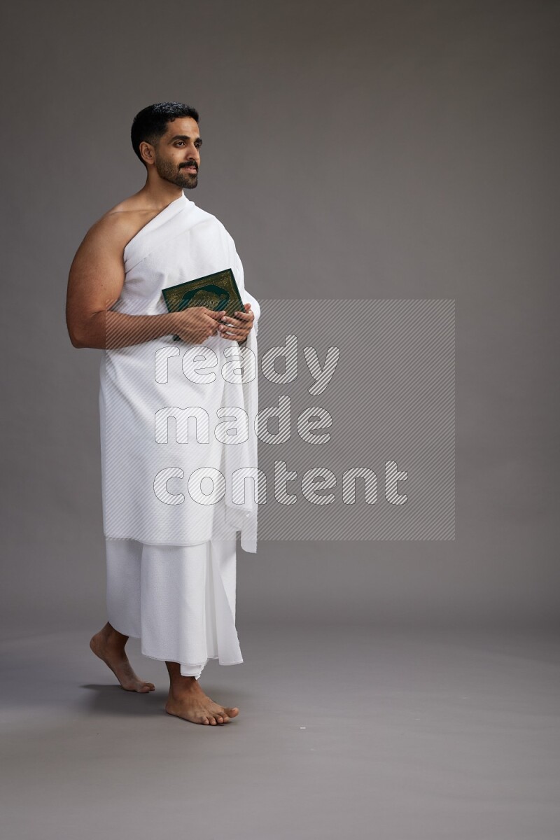 A man wearing Ehram Standing reading quran on gray background