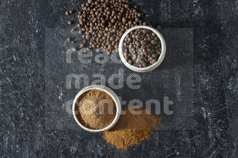 2 beige bowls, one full of allspice powder and the other full of whole balls and both spread on a textured black flooring