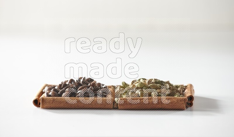 مربعان من أعواد القرفة ممتلئان بحبوب الهيل وحبوب القهوة علي خلفية بيضاء