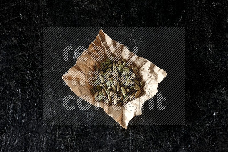Cardamom seeds in a crumpled piece of paper on textured black flooring