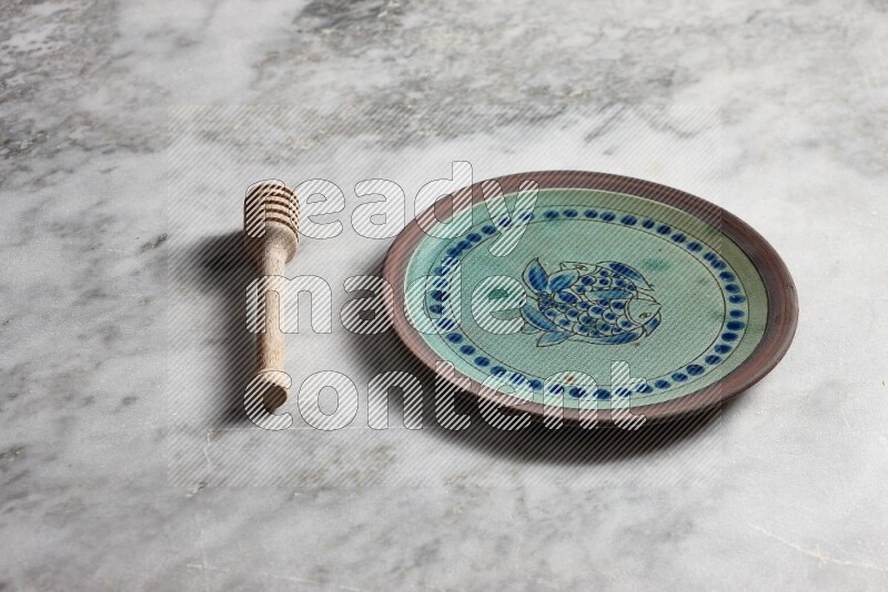 Decorative pottery plate with wooden honey dipper on the side on grey marble background