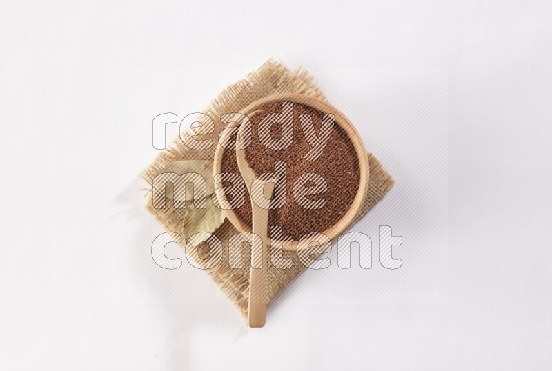 A wooden bowl and spoon full of garden cress seeds on burlap fabric on a white flooring