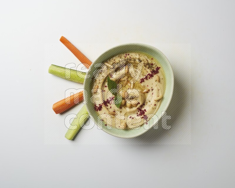 Hummus in a green plate garnished with zattar & sumak on a white background