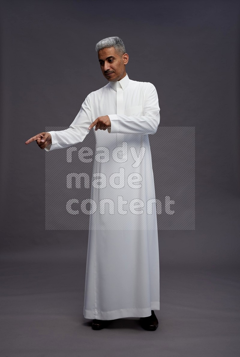 Saudi man wearing thob standing interacting with the camera on gray background