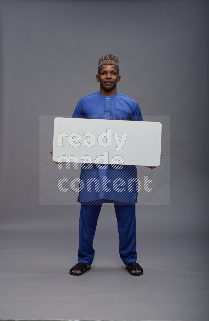 Man wearing Nigerian outfit standing holding board on gray background