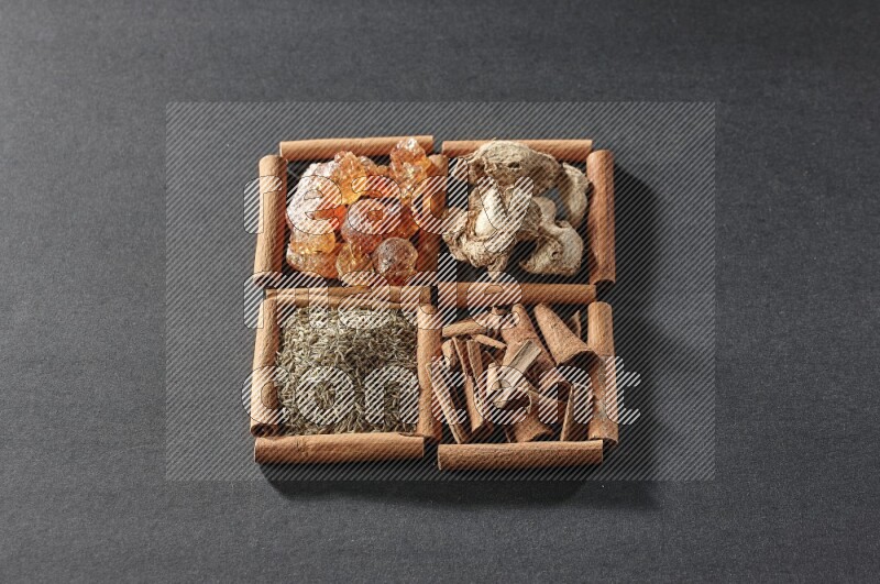 4 squares of cinnamon sticks full of gum arabic, dried ginger, cinnamon and cumin on black flooring