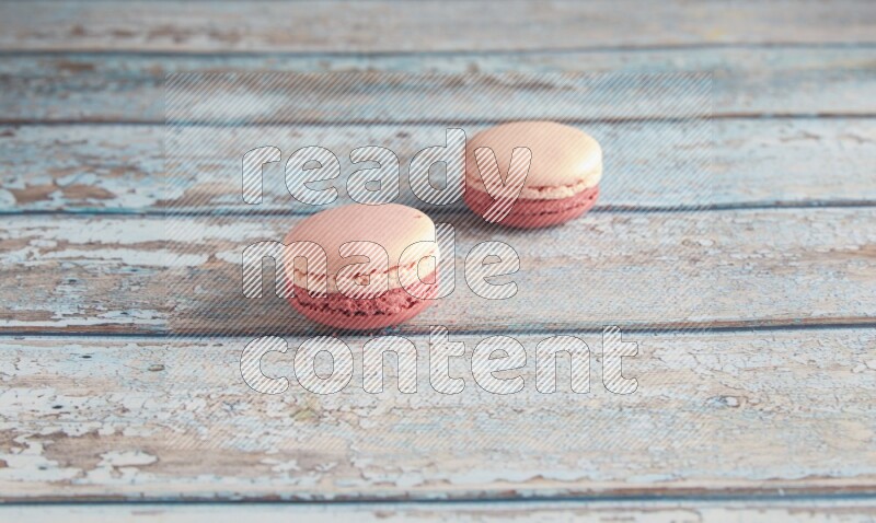 45º Shot of two Pink Litchi Raspberry macarons on light blue wooden background