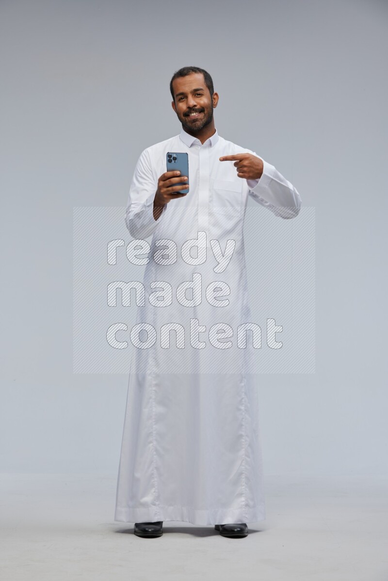 Saudi man wearing Thob standing texting on phone on Gray background