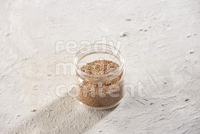 A glass jar full of mustard seeds on a textured white flooring