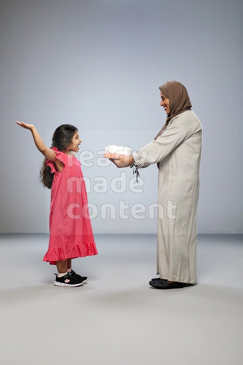 A mother giving a cake to her daughter on gray background