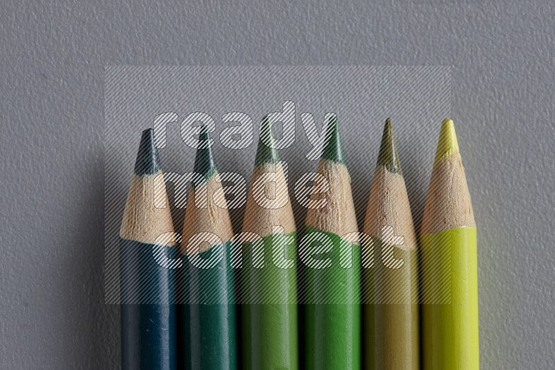 A collection of colored pencils arranged showcasing a gradient of green hues on grey background