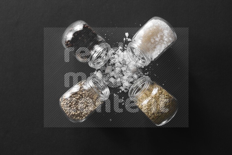 ملح وفلفل أسود وفلفل أبيض وكمون في أوعية زجاجية علي خلفية سوداء