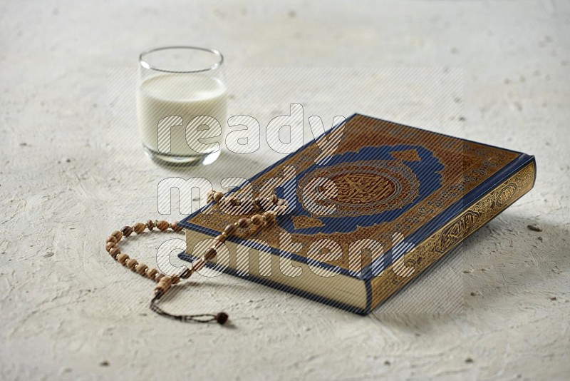 Quran with dates, prayer beads and different drinks on textured white background