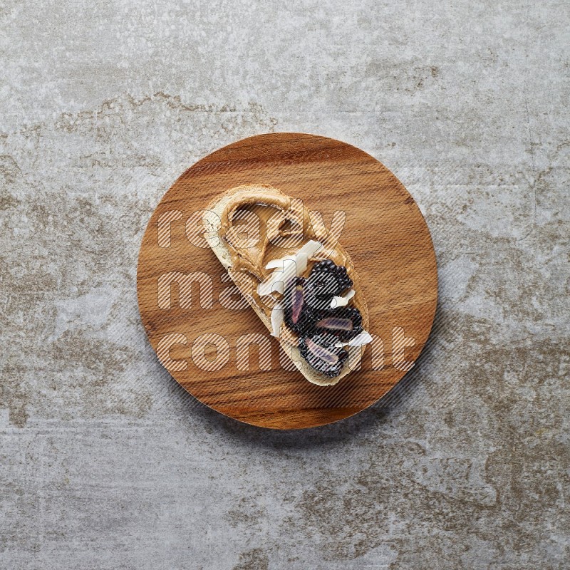 open faced peanut butter sandwich with blackberries  and coconut flakes on a  grey textured background