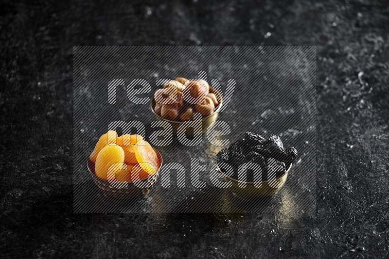 Dried fruits in metal bowls in a dark setup