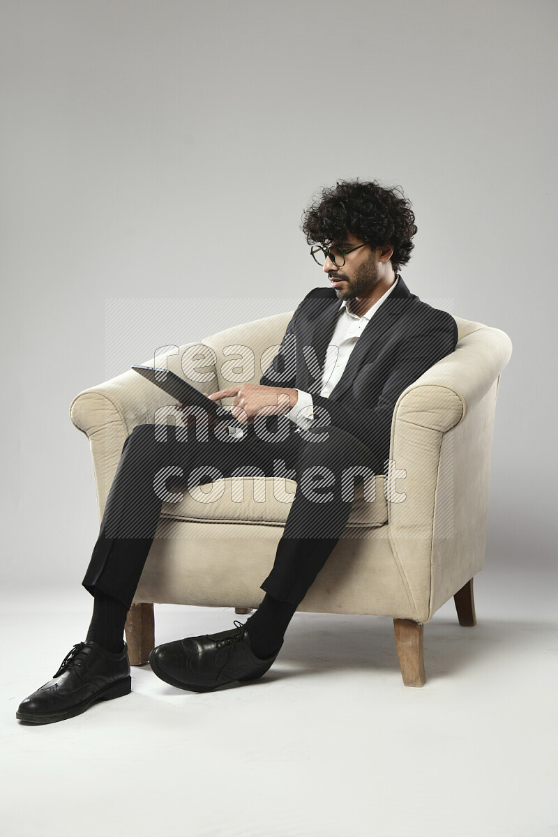 رجل يرتدي ملابس رسمية يجلس علي كرسي و يتصفح تابلت علي خلفية بيضاء
