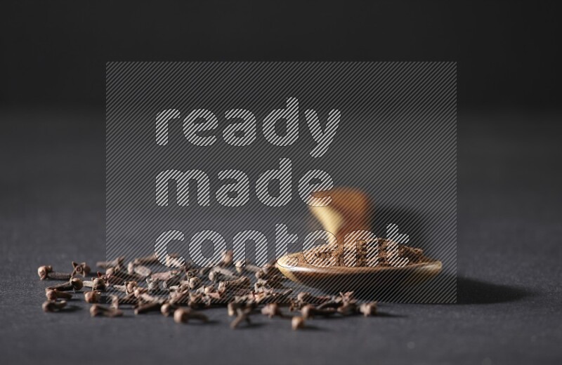 مغرفة خشبية ممتلئة ببودرة القرنفل مع بعض حبوب القرنفل الكاملة حولها على خلفية سوداء