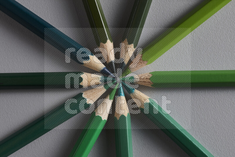 An arrangement of colored pencils in shades of green on grey background