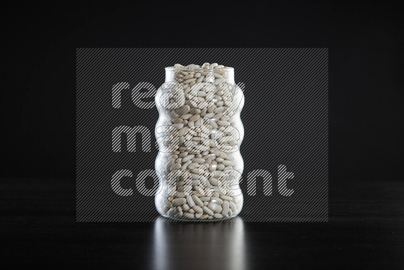 White beans in a glass jar on black background