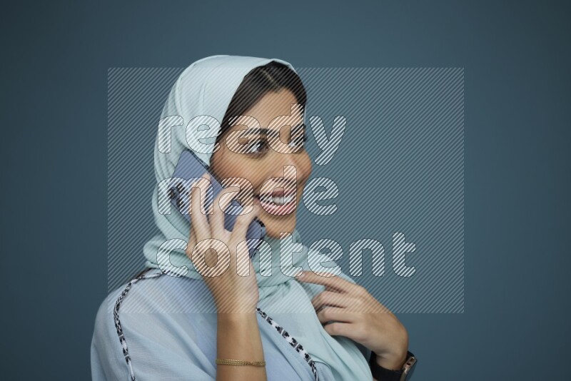 A Saudi woman having a Call in a blue background wearing blue Abaya with hijab