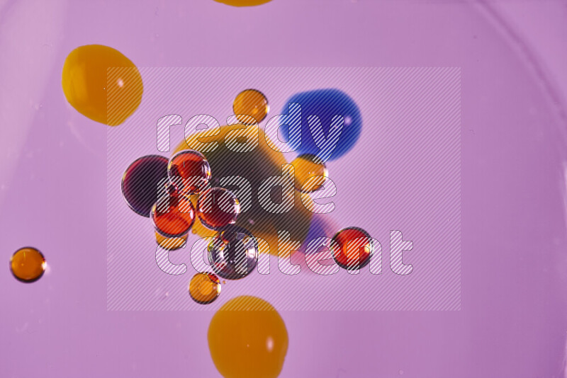 Close-ups of abstract red, blue and yellow watercolor drops on oil Surface on pink background