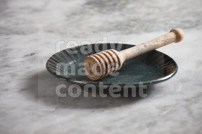 Multicolored pottery plate with wooden honey dipper in it on grey marble background
