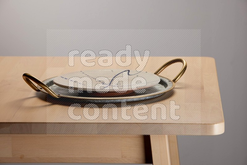 multicolored plate placed on a rounded stainless steel tray with golden handels on the edge of wooden table