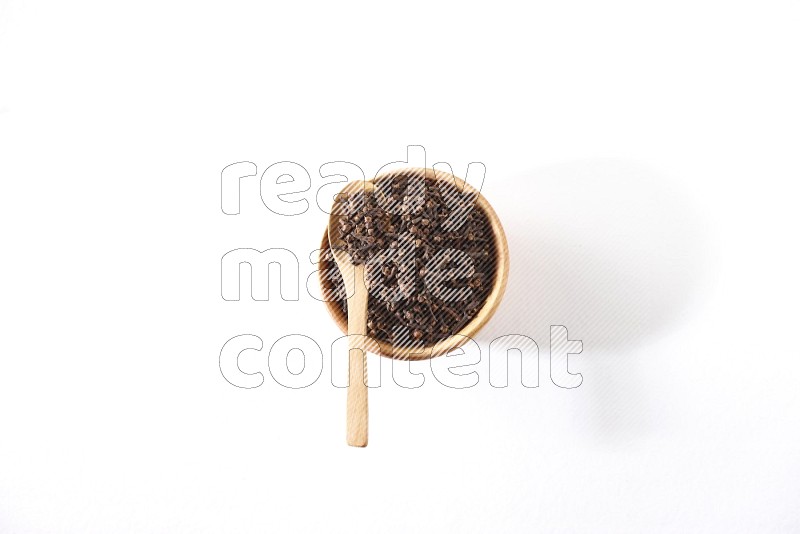 A wooden bowl and a wooden spoon full of cloves on a white flooring