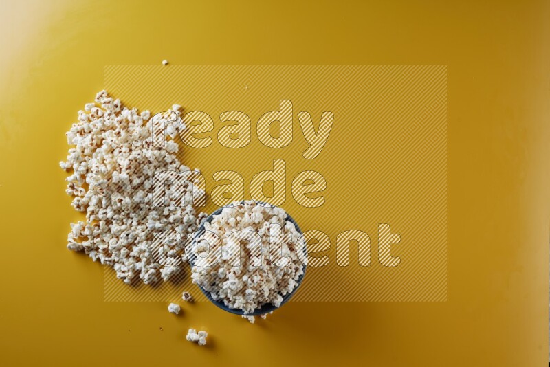 A blue pottery bowl full of popcorn with popcorn beside it on a yellow background in different angles