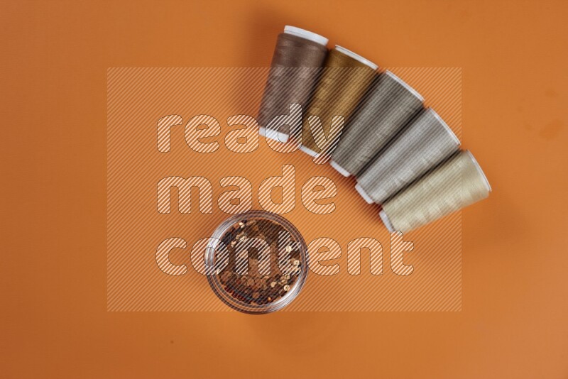 مجموعة من أدوات الخياطة والتفصيل بنية اللون على خلفية برتقالية