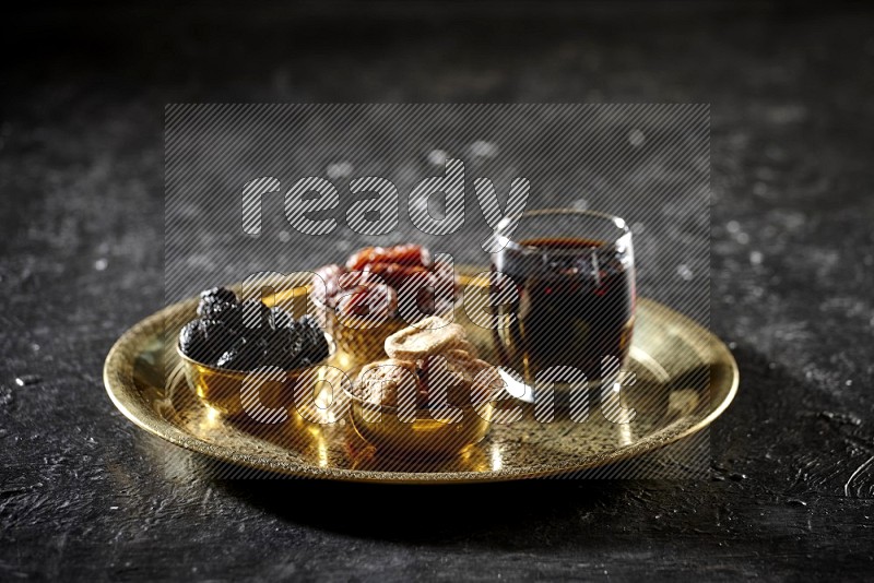 Dried fruits in metal bowls with tamarind on a tray in dark setup