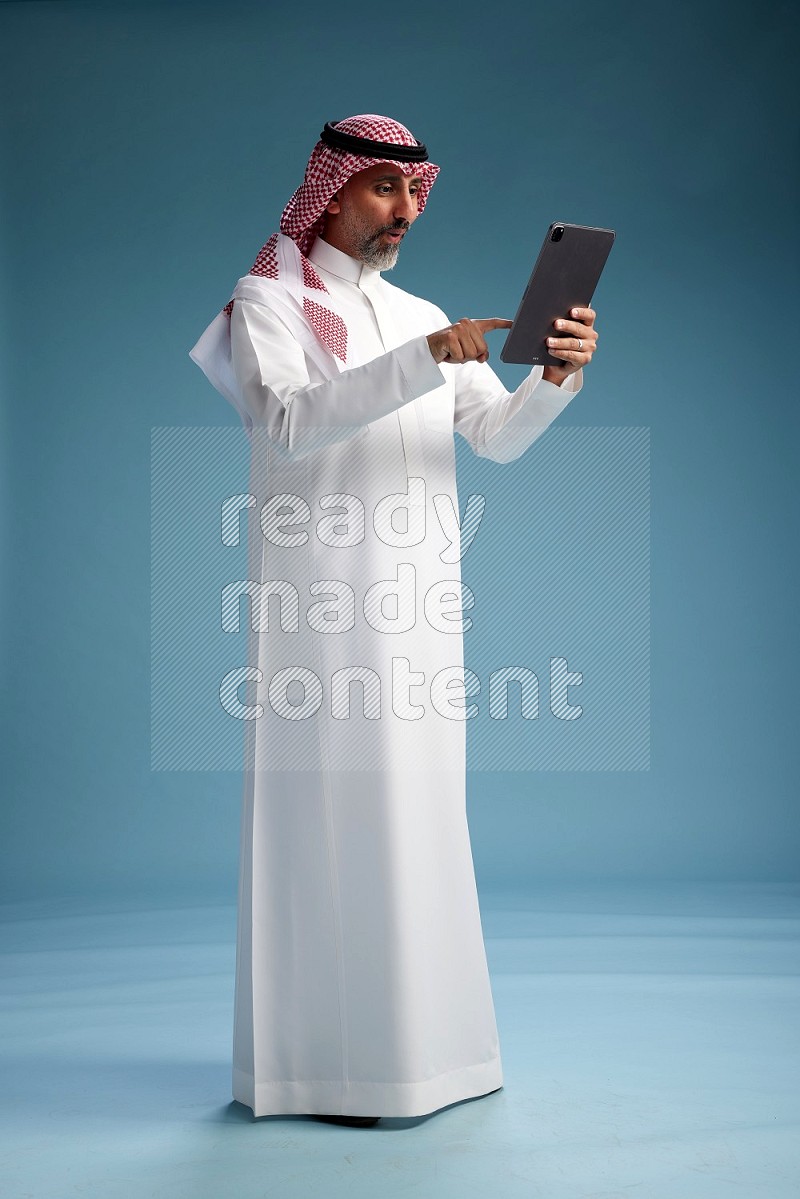 Saudi man wearing thob and shomagh with tablet on Blue background