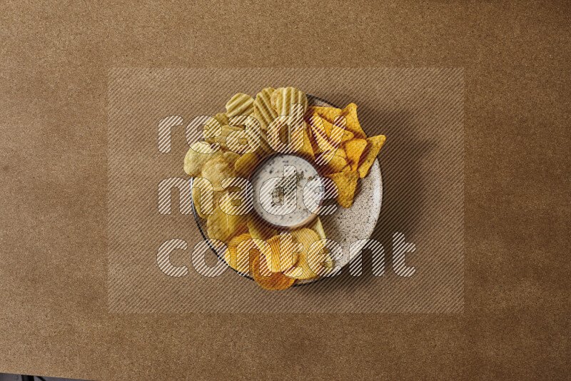 Assorted snacks on a pottery plate with a dipping on brown background