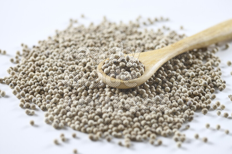 White pepper beads with wooden spoon on white background