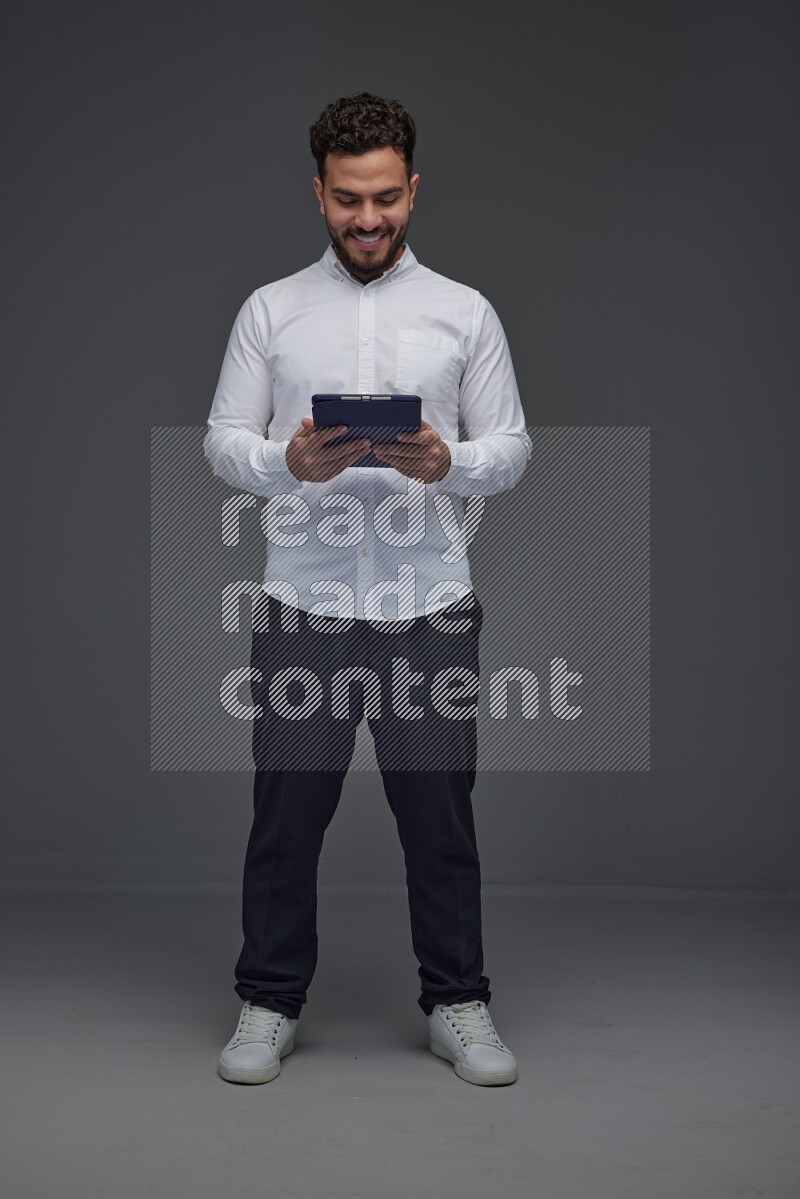 A man wearing smart casual standing and using his tablet eye level on a gray background
