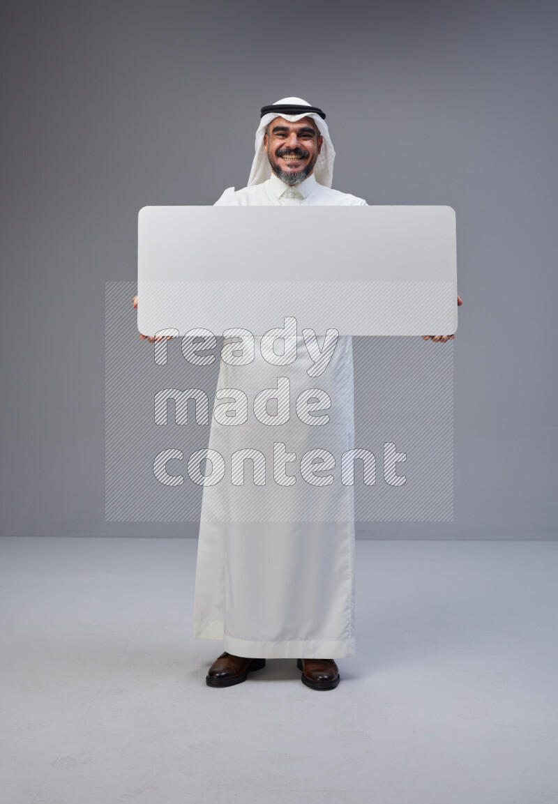 Saudi man Wearing Thob and white Shomag standing holding board on Gray background