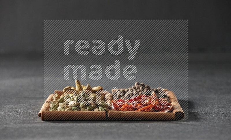 4 مربعات من عيدان القرفة ممتلئة بحبوب الهيل والفلفل الحار وبهار الفلفل الحلو وأصابع الكركم على أرضية سوداء