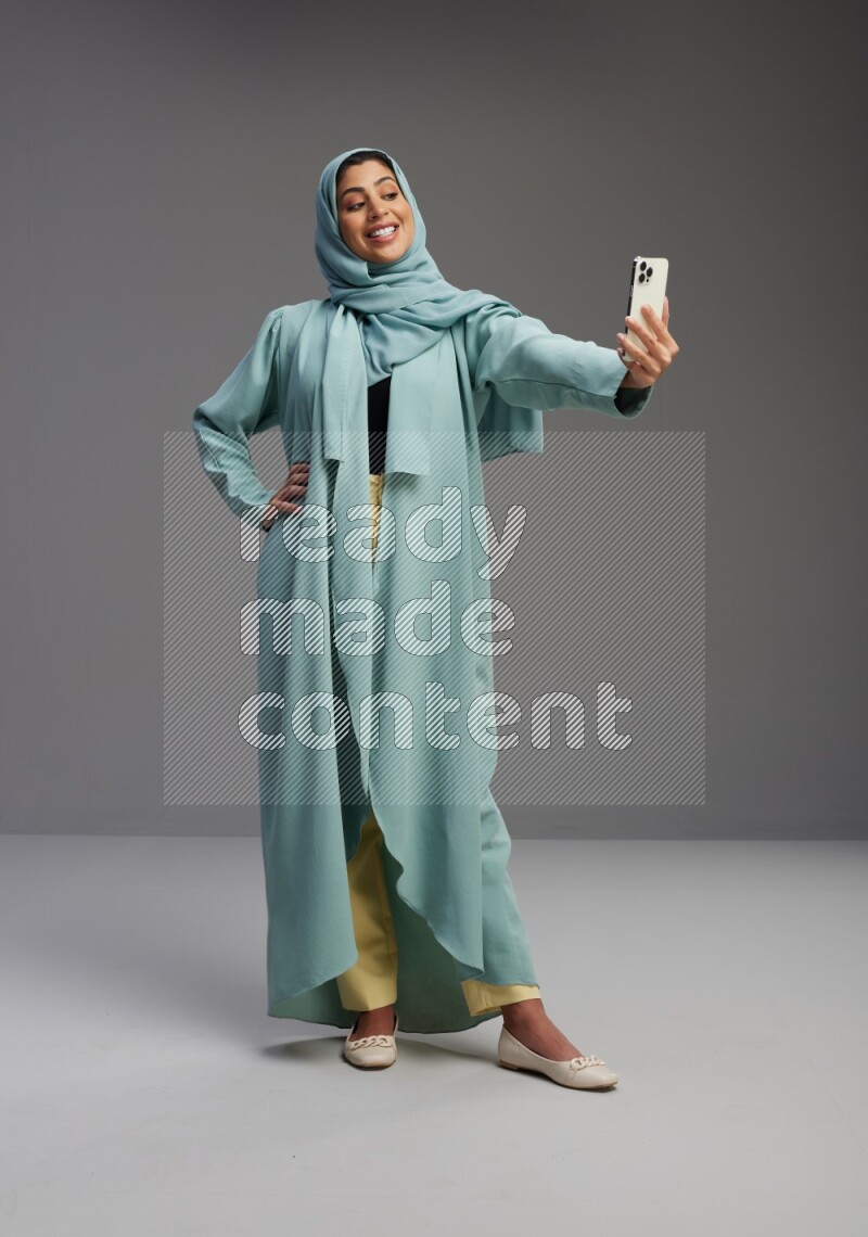 Saudi Woman wearing Abaya standing taking selfie on Gray background