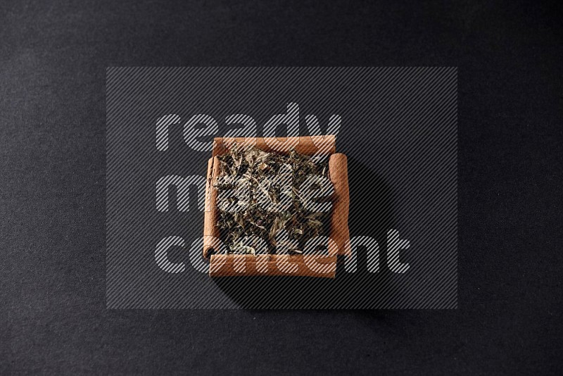 A single square of cinnamon sticks full of dried basil on black flooring