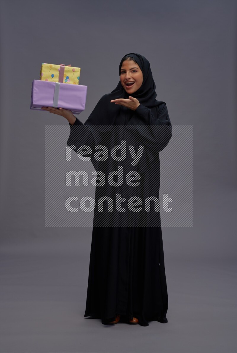 Saudi woman wearing Abaya standing holding gift box on gray background