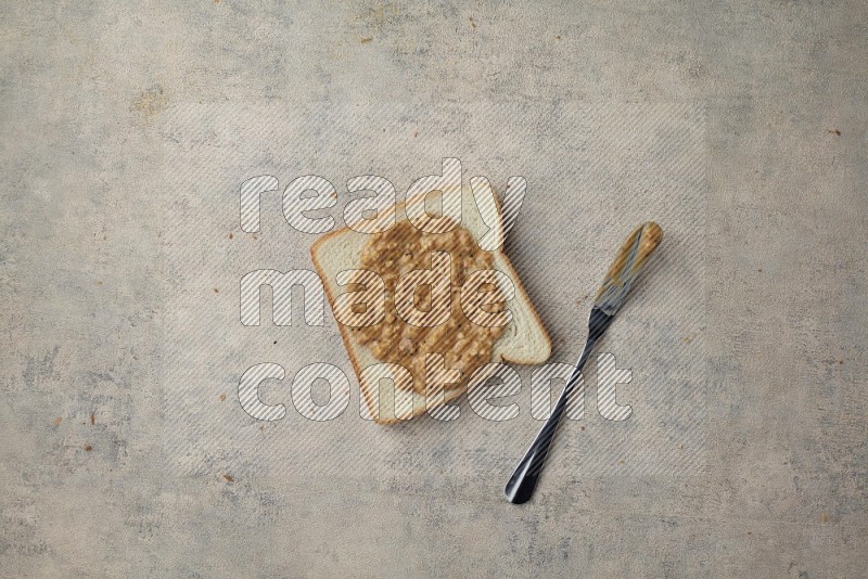 crunchy peanut butter on a white toast with a spreading knife on a light blue textured background