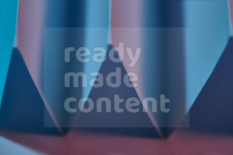 صورة مجردة مقربة تظهر طيات ورقية هندسية حادة بتدرجات اللون الأزرق والوردي