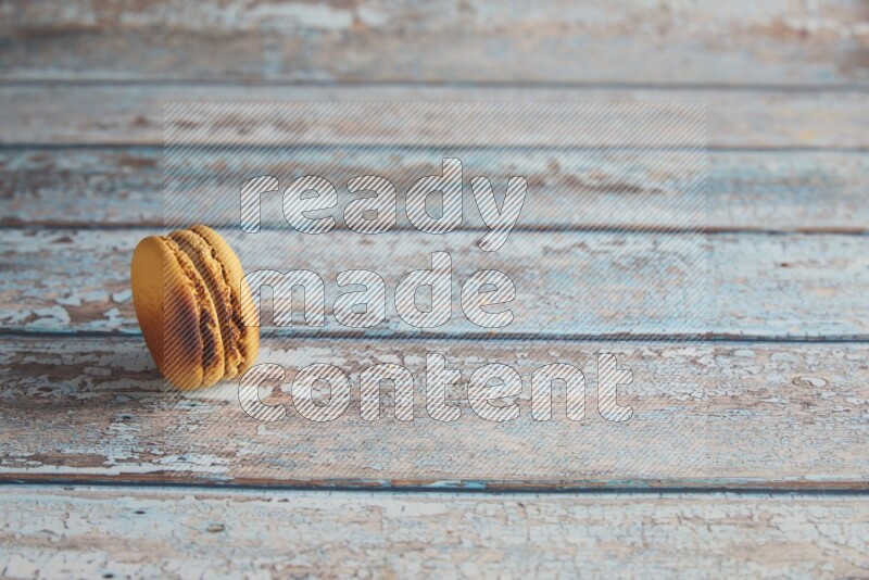 45º Shot of Yellow Crème Brulée macaron on light blue wooden background