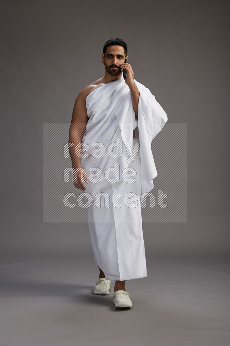 A man wearing Ehram Standing talking on phone on gray background