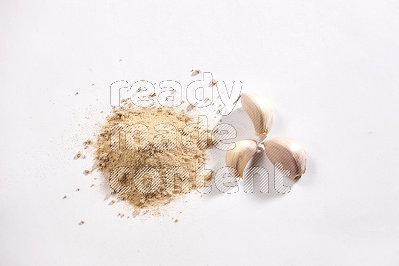 A small pile of garlic powder with some of cloves and a whole garlic bulb on a white flooring