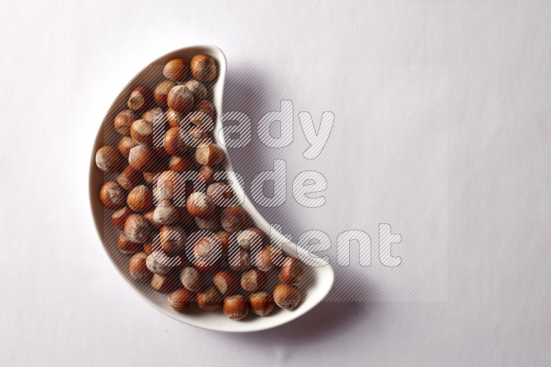 Hazelnuts in a crescent pottery plate on white background