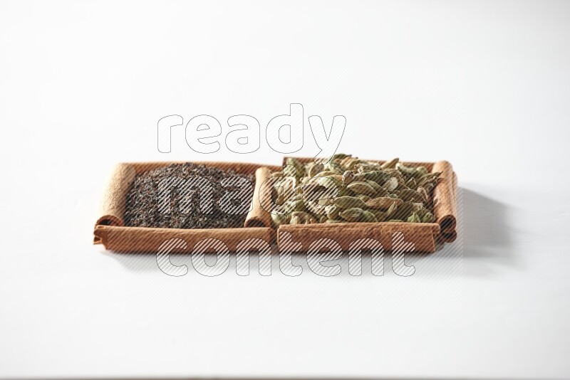 مربعان من أعواد القرفة ممتلئان بحبوب الهيل والشاي الأسود علي خلفية بيضاء