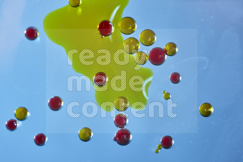 Close-ups of abstract yellow and red watercolor drops on oil Surface on blue background